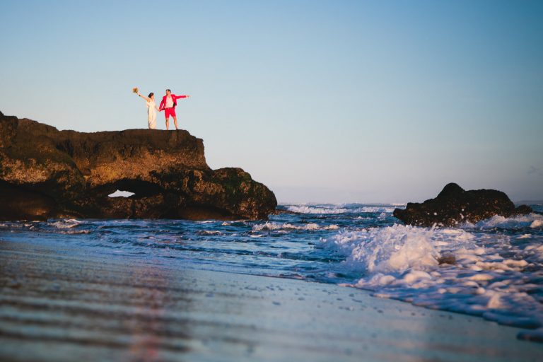 bride and groom standing on ocean rocks at sunset in bali