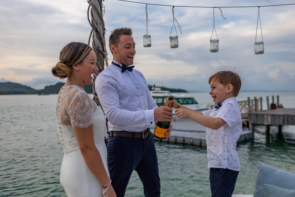 bride and groom and their son open a bottle of champagne after their wedding ceremony at Song Saa Private Island in Cambodia
