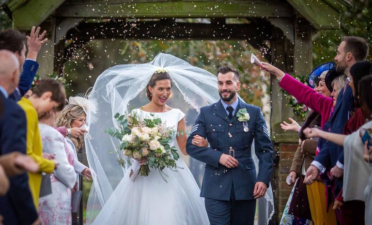 bride and groom leave the church after their wedding ceremony in Lincoln England with guests throwing confetti by associate photographer aidan dockery