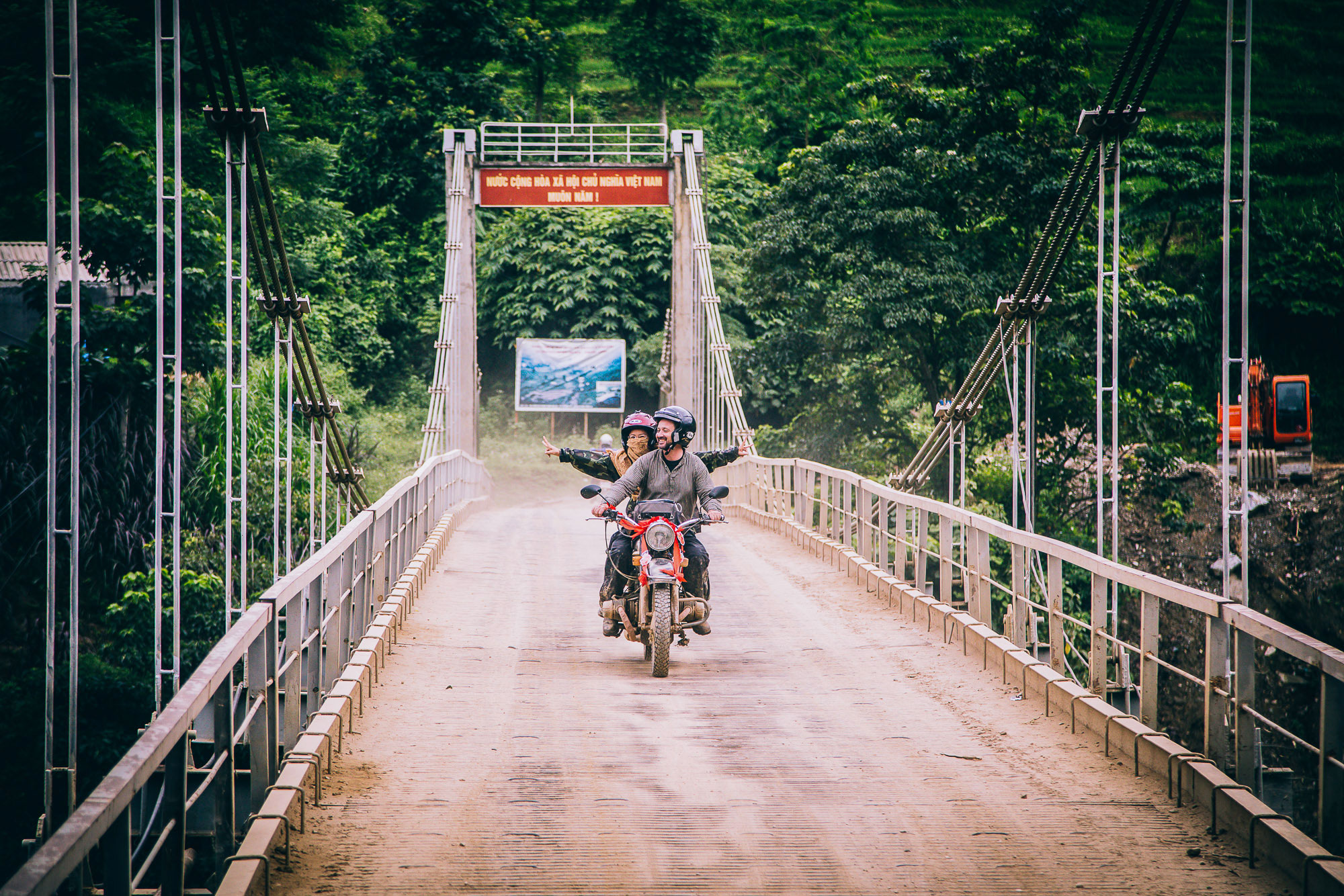 bride and groom on motorbike cross a bridge on way to the vietnam wedding